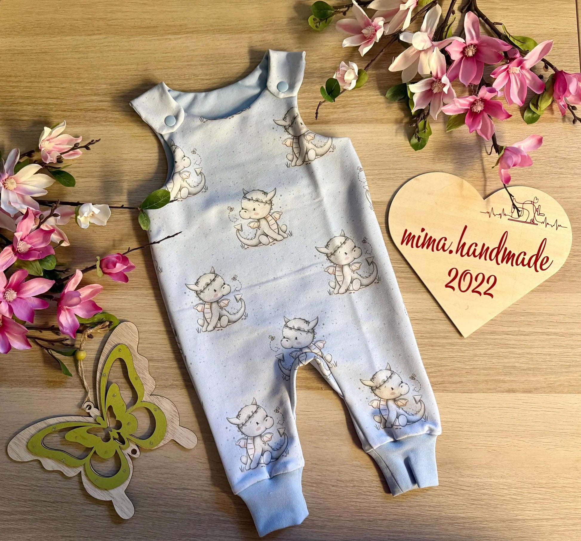 1. Baby Strampler Größe 62 in Blau mit Drachenmotiv aus French Terry, flach liegend fotografiert
