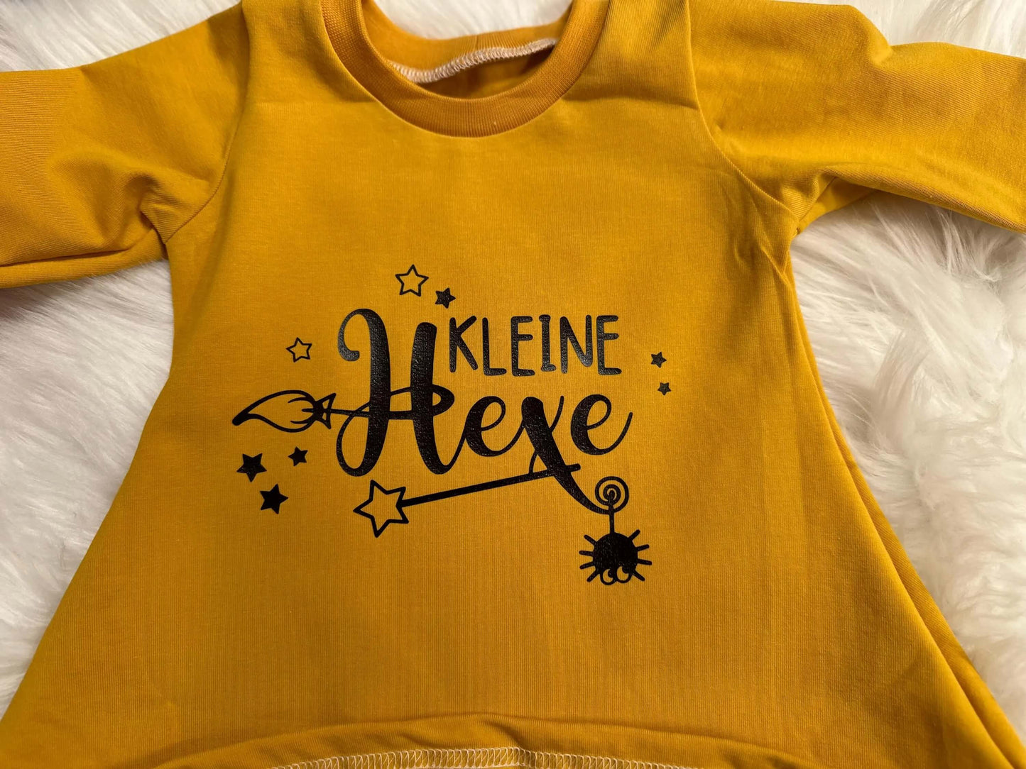 Detailaufnahme des „Kleine Hexe“ Schriftzugs auf gelbem Kleid
