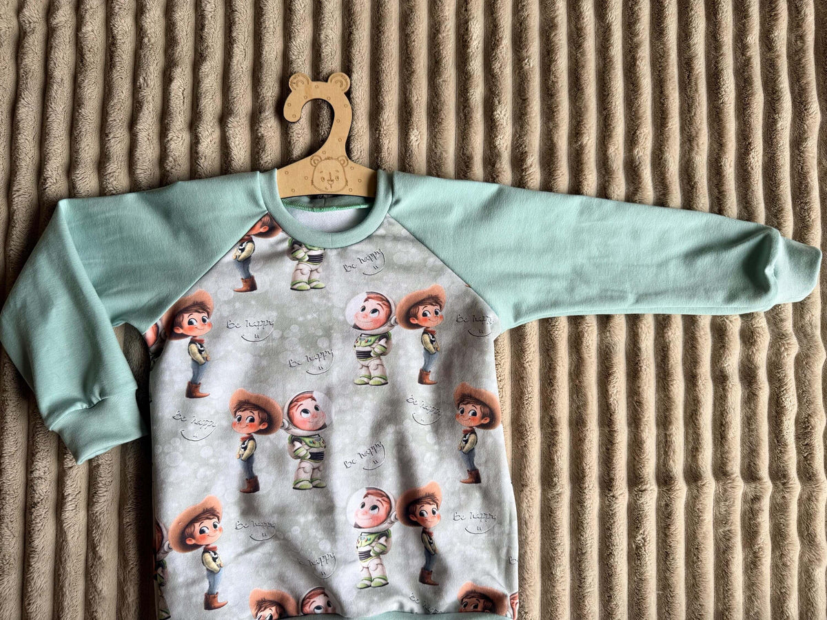 Raglan Pullover Kinder Größe 98 grün mit Spielzeugfreunde-Motiv, am Kleiderbügel fotografiert