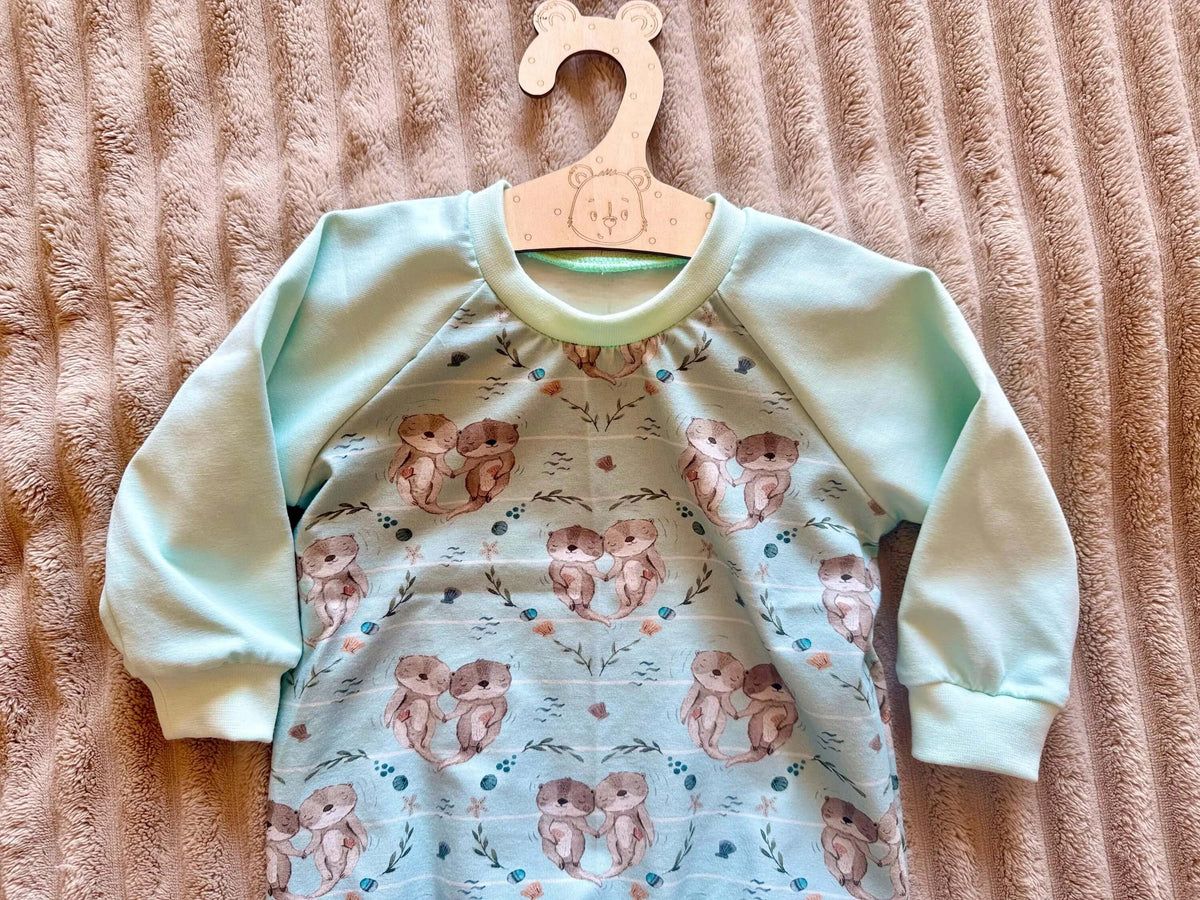 Raglan Pullover Baby Größe 74 türkis mit Otter-Print, am Kleiderbügel fotografiert