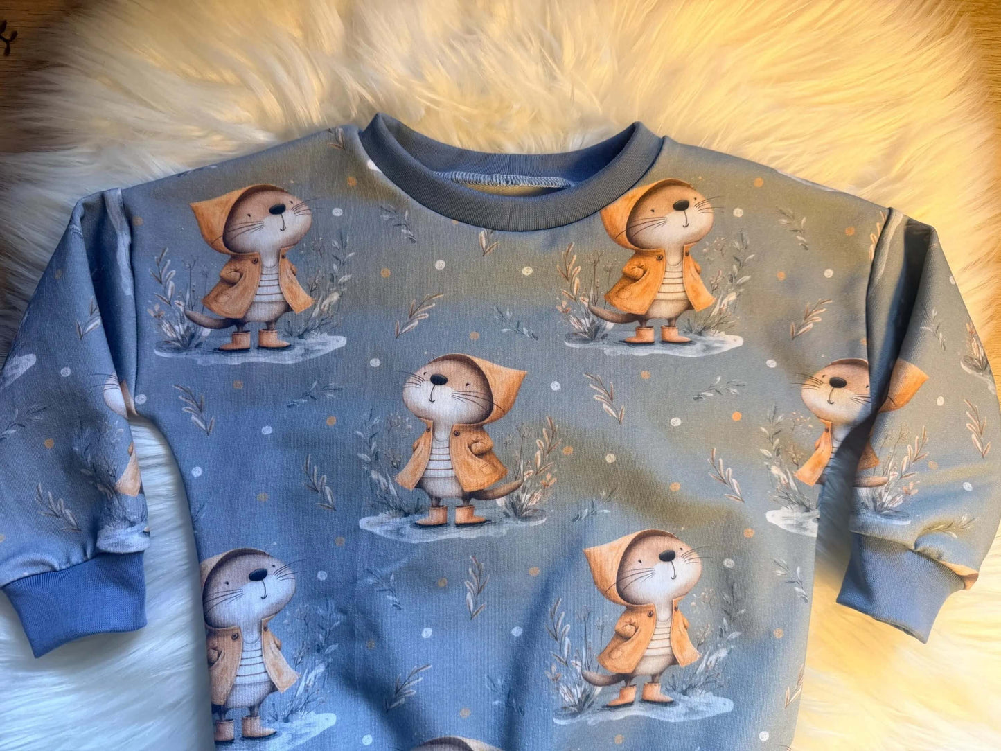 „Kinderpullover mit Hals-, Arm- und Saumbündchen – Otter im Regenmantel“