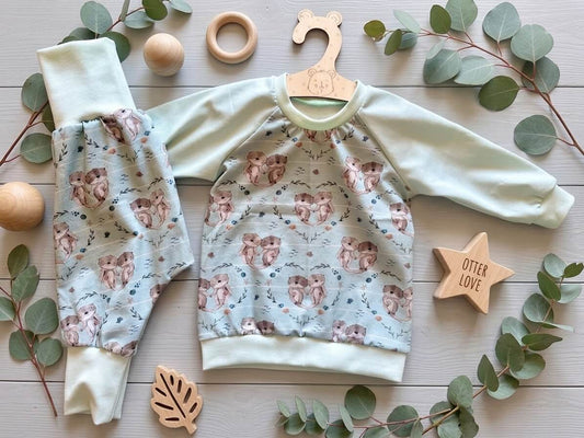 Set Raglan Pullover und Pumphose Baby Größe 74 türkis mit Otter-Motiv, Jersey, flach liegend mit Holzspielzeug