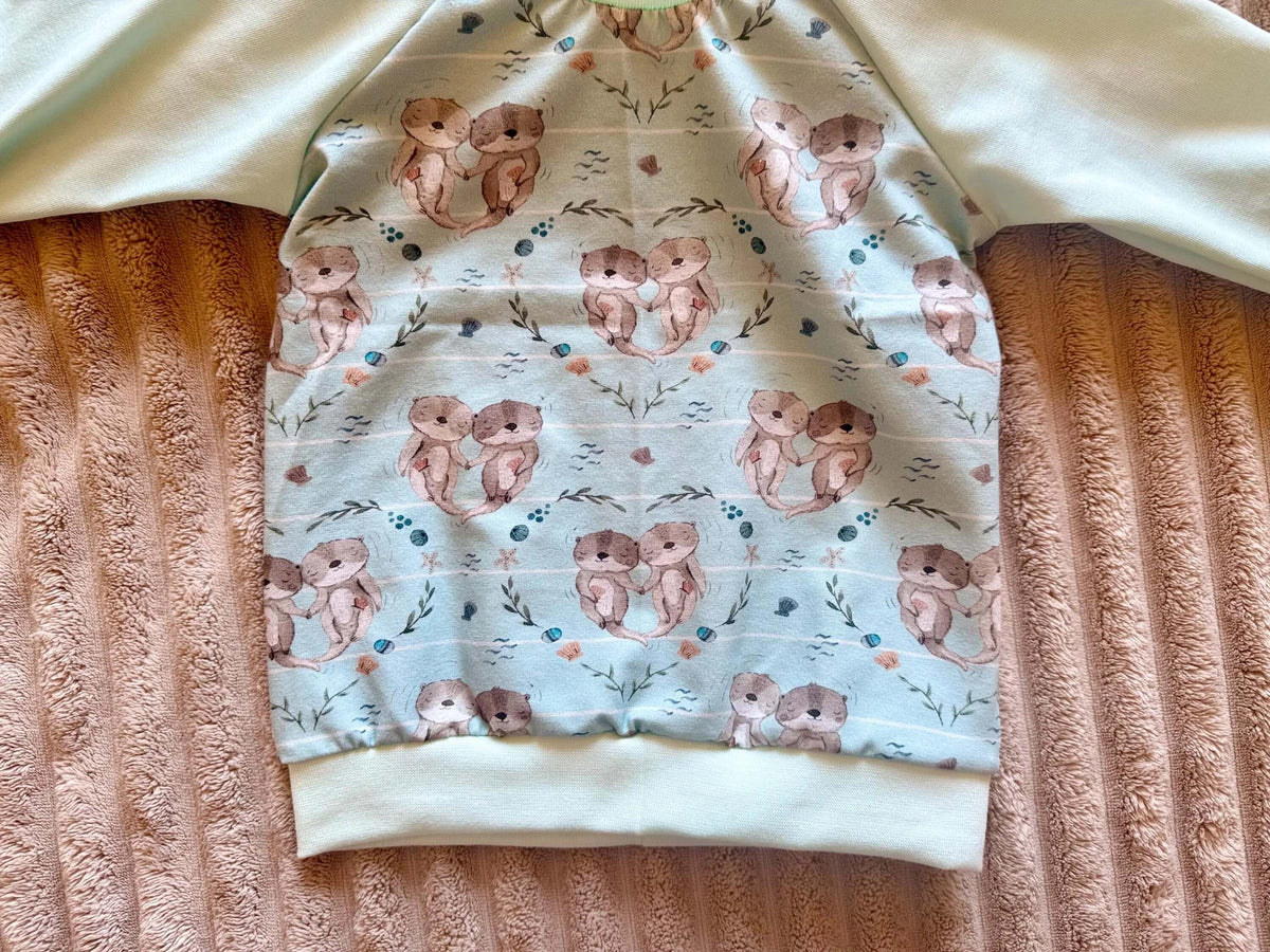 Nahaufnahme niedliches Otterpärchen-Muster auf türkisem Jersey Pullover Gr. 74
