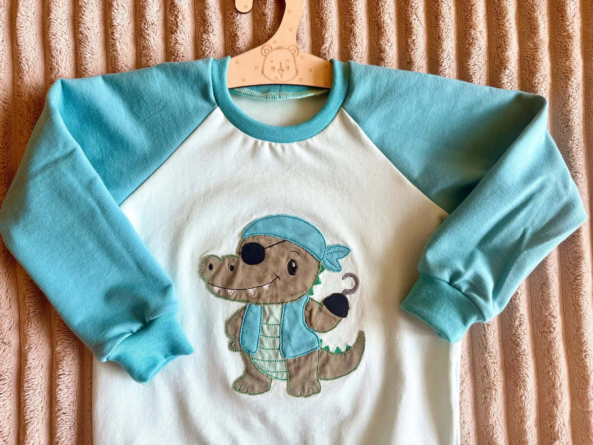 Pullover Kinder Größe 98 türkis mit Piraten-Krokodil-Motiv, am Kleiderbügel fotografiert
