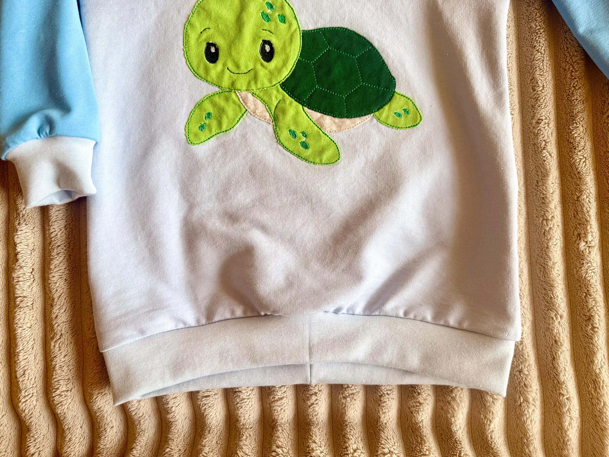 Nahaufnahme Stickapplikation Schildkröte auf blauem Jersey Pullover Gr. 98