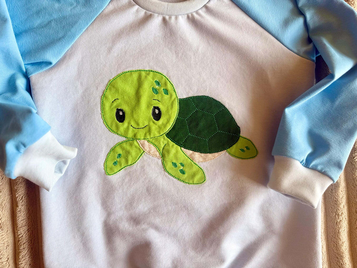 Detailansicht Schildkröten-Stickapplikation und blaues Saumbündchen am Pullover Gr. 98