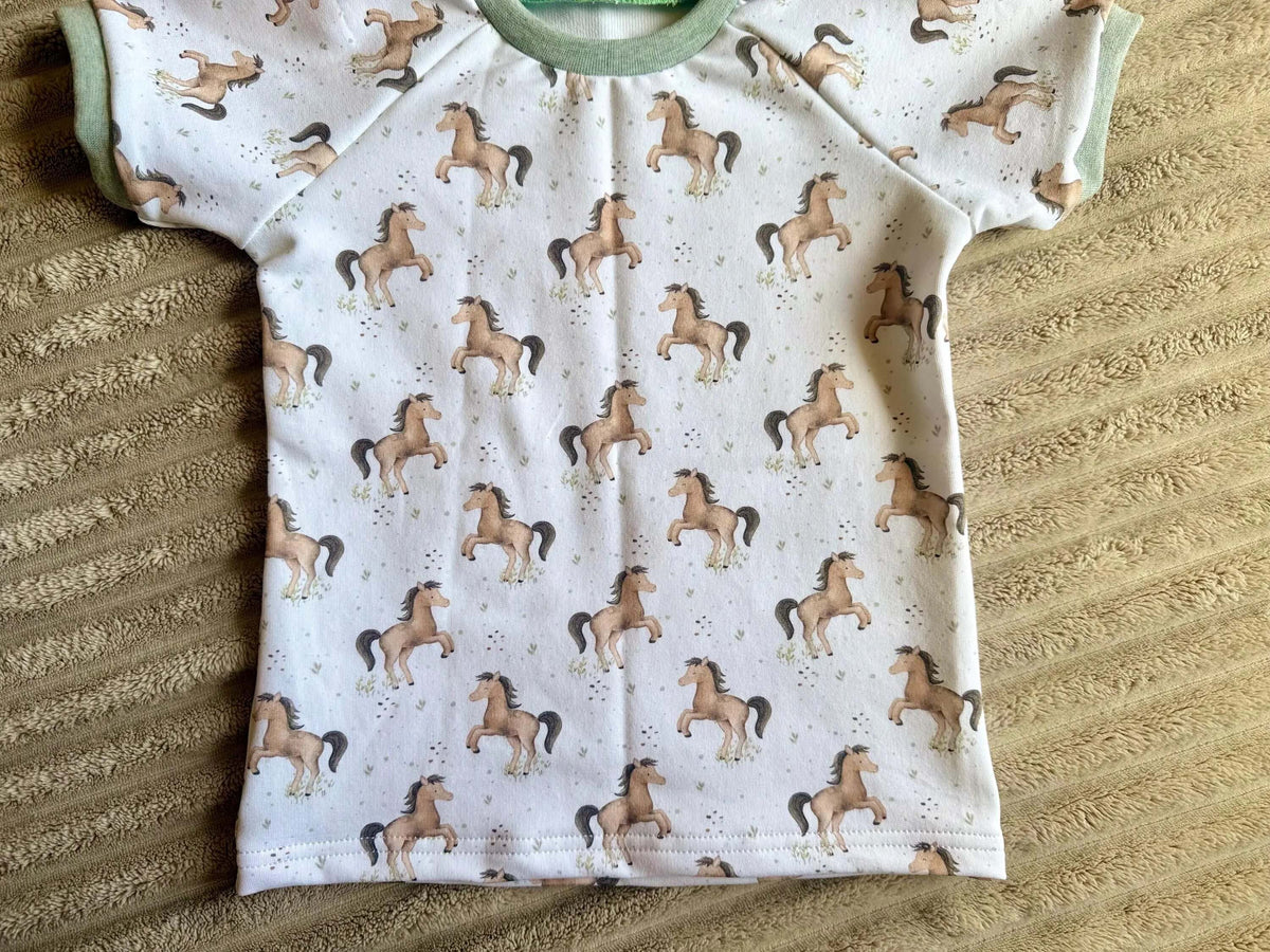 Rock Kinder Größe 98 weiß mit Kleine-Pferde-Muster und grünem Bauchbündchen, flach liegend fotografiert